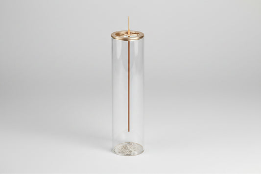 Clear cylindrical glass holder with a gold rim containing an incense stick on a white background