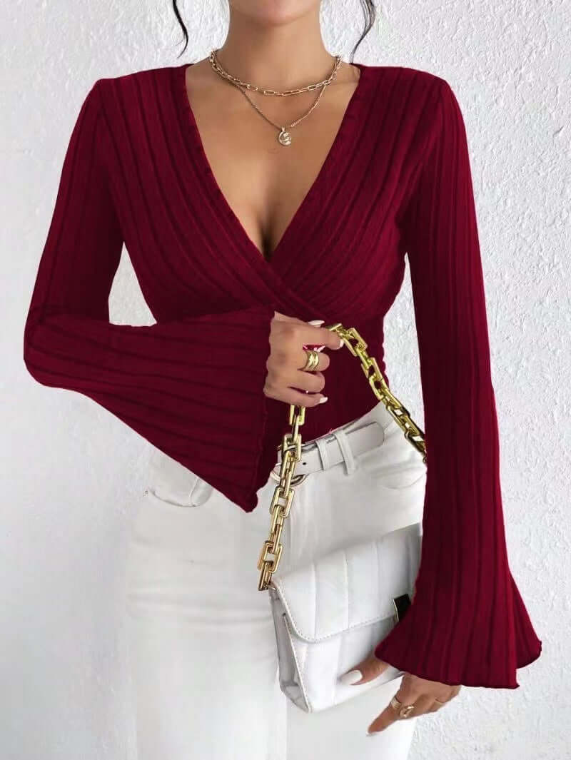 Women's V-neck long sleeve top in burgundy with ribbed pattern and bell sleeves, styled with white pants and handbag.