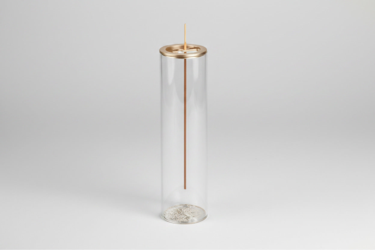 Clear cylindrical glass holder with a gold rim containing an incense stick on a white background