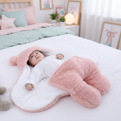 Baby wrapped in a pink and white fluffy blanket with a matching hat on a light background