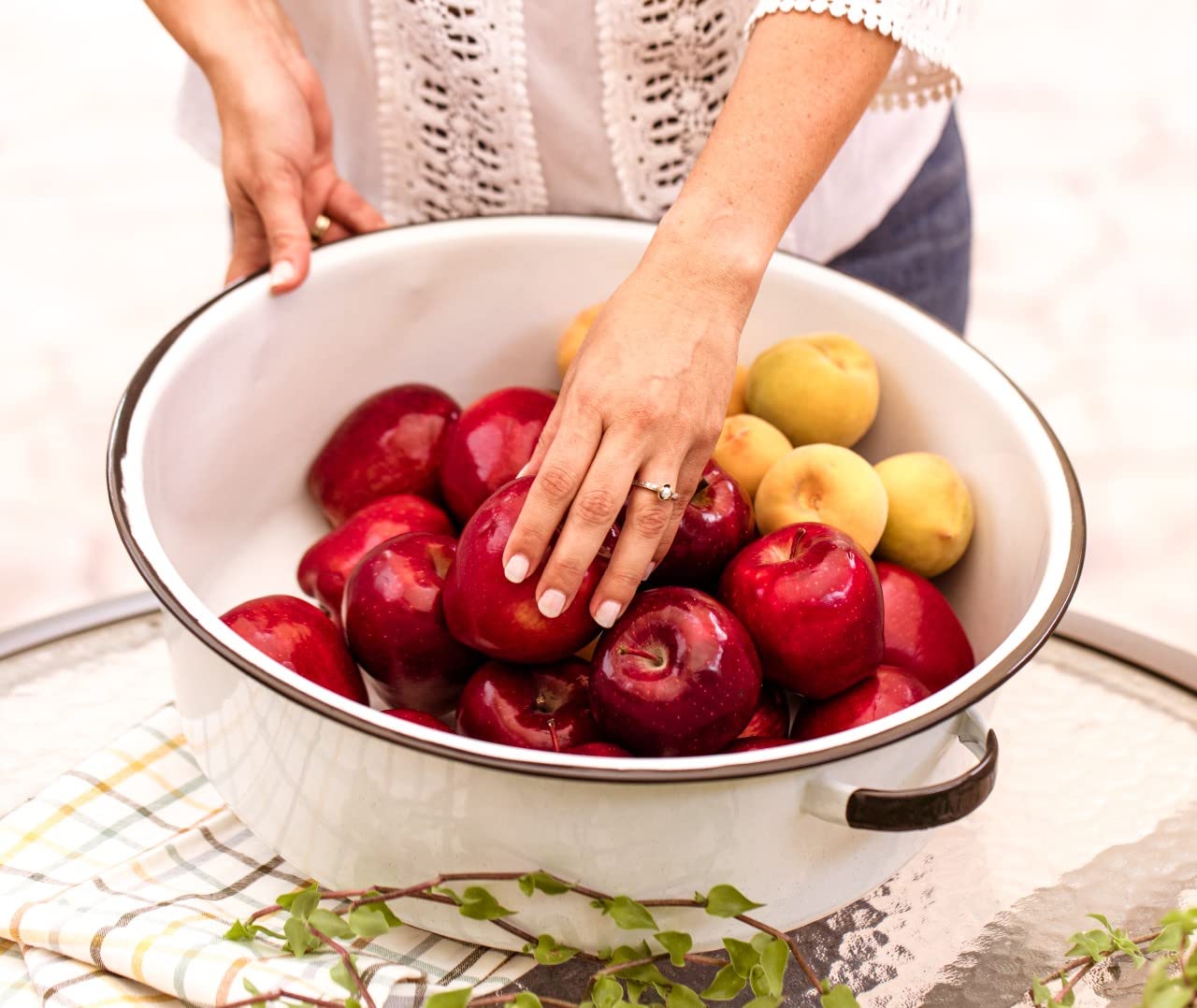 Person holding a bowl of red and yellow plums on a white background