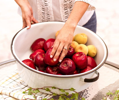 Person holding a bowl of red and yellow plums on a white background