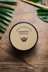 Beard balm container labeled 'Ironwood' on a wooden surface with leaves in the background
