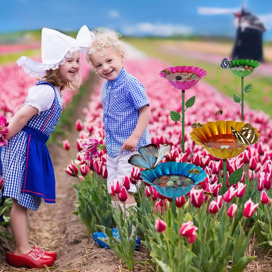 Two children smiling in a tulip field beside colorful metal bee flower watering stations for pollinators.