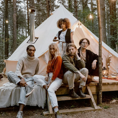 Group of people sitting in front of a tipi tent in a forest setting