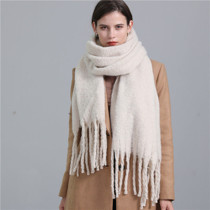 Woman wearing a beige scarf with tassels against a gray background