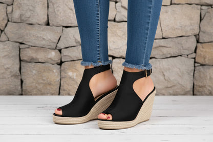 Black wedge sandals with open toes on a light wooden floor.