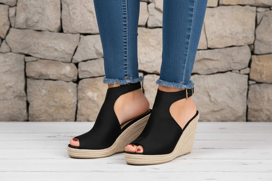 Black wedge sandals with open toes on a light wooden floor.