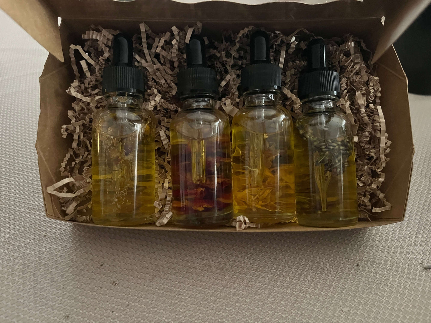 Four dropper bottles with liquids in a cardboard box on a plain surface