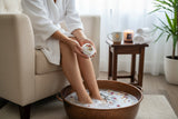 Therapeutic Foot Soak Bombs being held above a warm foot bath by a person in a cozy setting.