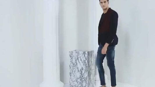 Stylish man wearing casual leather shoes with blazer and jeans, posed elegantly near a marble pedestal.